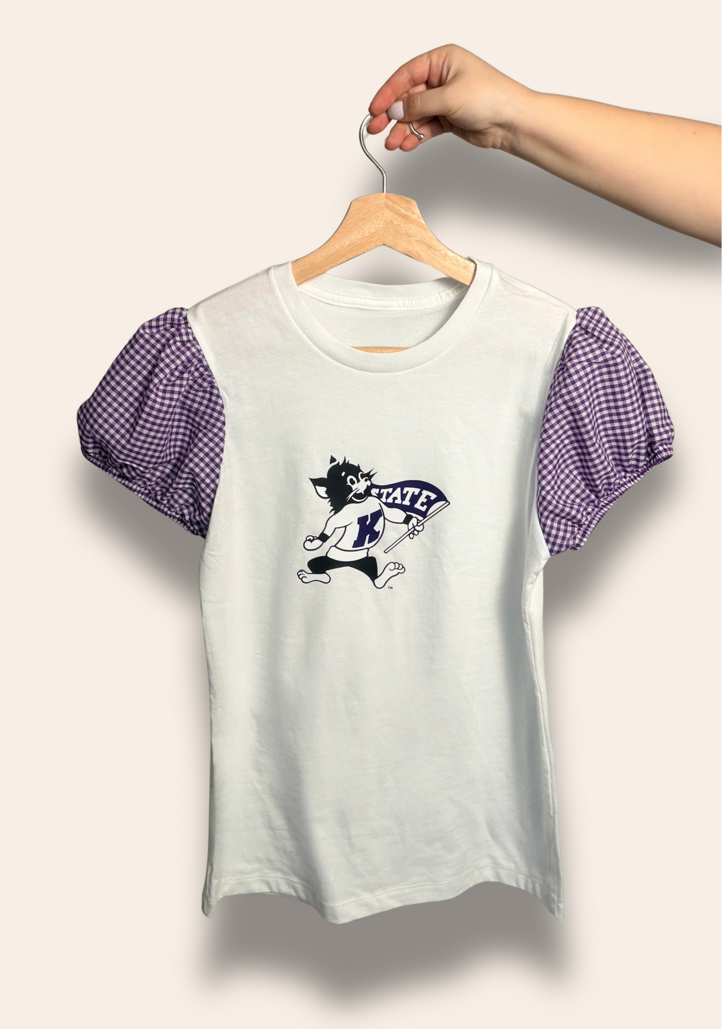 Classic Wildcats, but make it cute.
Our K-State Gingham Puff Tee features a timeless white base with the iconic Wildcat front and center, paired with the sweetest purple gingham puff sleeves. Feminine, flattering, and full of K-State pride, it’s perfect for game days, campus strolls, and cheering on the Cats in style.
Comfortable, elevated, and made for the cutest fan in the stands.