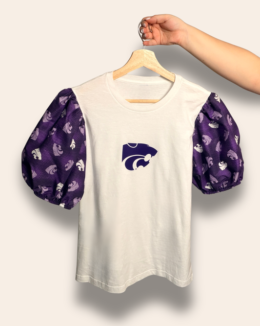 Our K-State Classic Puff Tee features a crisp white body with dreamy purple puff sleeves and the iconic Wildcat front and center. It’s the perfect mix of feminine and fierce, made for tailgates, campus days, and cheering on the Cats in style.

Comfortable, flattering, and guaranteed to get compliments.
