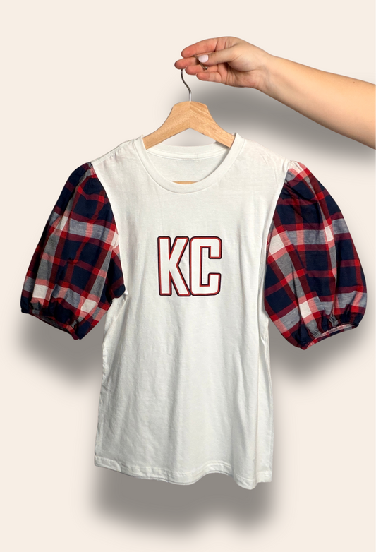Game day, but make it cute.

Our KC Classic Plaid Puff Tee features bold KC lettering and statement red and blue plaid puff sleeves for the perfect mix of sporty and feminine. It’s cozy, flattering, and made for cheering on Kansas City in style from tailgate to touchdown.

Comfortable, eye-catching, and made for your KC era.