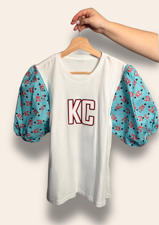For the girls who cheer loud and dress cute doing it.

Our KC Current Sweetheart Puff Tee features a classic white base with bold KC lettering and dreamy teal puff sleeves covered in playful KC and heart details. It’s the perfect mix of feminine and fierce, made for match days, summer nights, and showing your Current pride in style.

Soft, flattering, and made to stand out in a sea of teal.