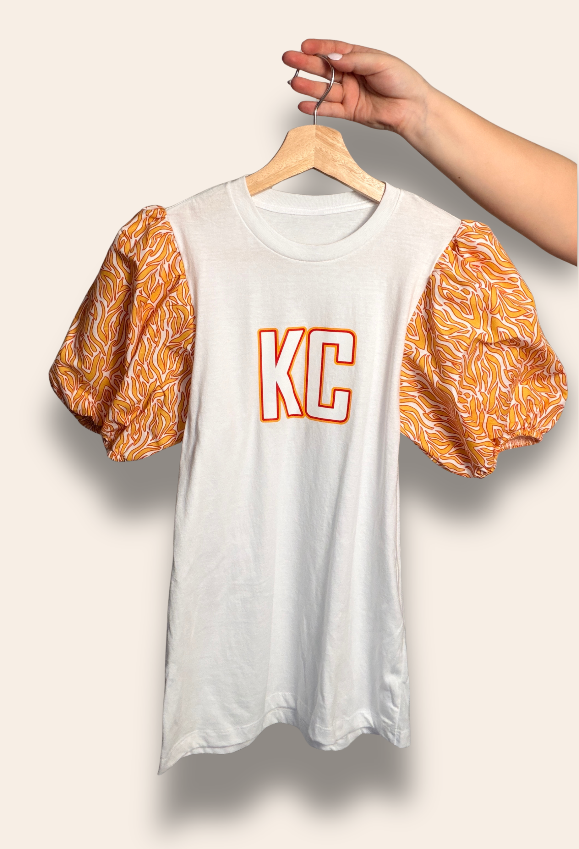 For the girls who belong to the Kingdom.

Our KC Kingdom Puff Tee features a classic white base with bold KC lettering and statement puff sleeves in vibrant red and gold tones. Feminine, bold, and made for game day, it’s the perfect top for tailgates, touchdowns, and cheering on Kansas City in style.

Comfortable, flattering, and made to stand out in a sea of red.